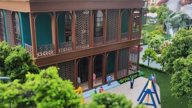 Balcony view of a detailed, multi-story building with lush greenery and children playing nearby.