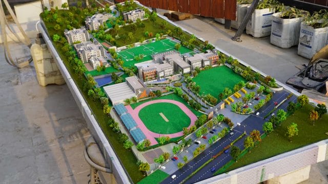 Detailed model of Shalom International School with sports fields and greenery.