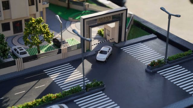 A lush green model entrance gate with pedestrian crosswalks and street lamps at the 66 Alaya by GBD.