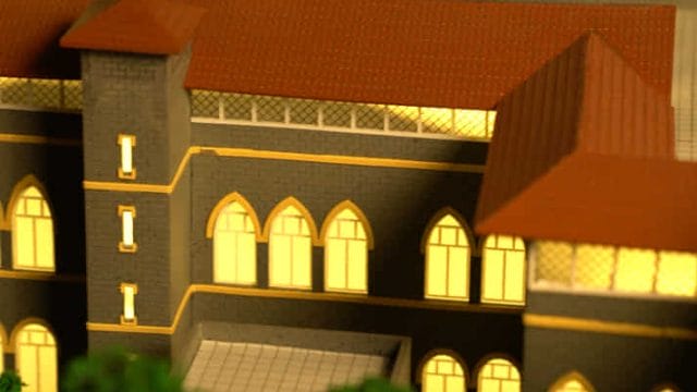 A detailed model of a historic building with illuminated windows, set against a dark background, rep.
