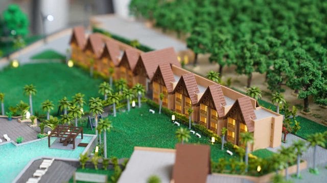 Modern tropical villa complex with lush gardens and pool, near green trees and outdoor seating areas.
